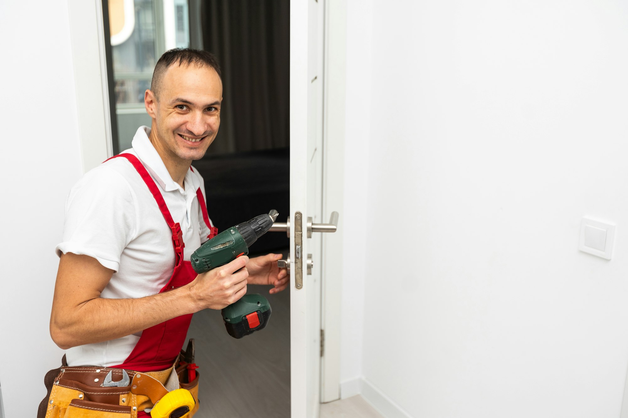 Cheerful locksmith installing a door lock on a new white door and looking at the camera